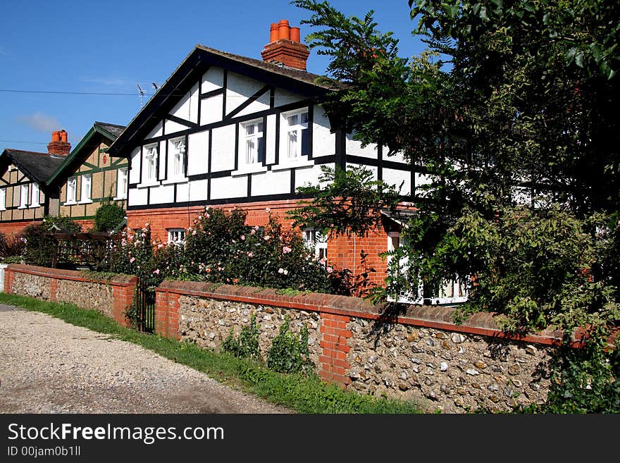 Row of Cottages in an English Rural Village with a brick and flint wall to the front and flowering rose bushes. Row of Cottages in an English Rural Village with a brick and flint wall to the front and flowering rose bushes