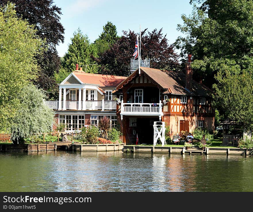 Boathouse and Dwelling on the Banks of the River Thames in England with people relaxing in the garden. Boathouse and Dwelling on the Banks of the River Thames in England with people relaxing in the garden
