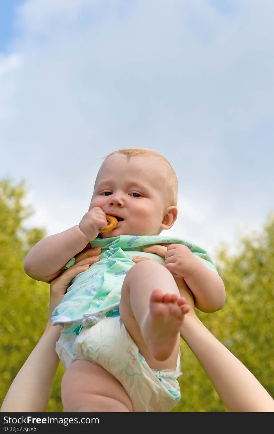 Small child on a background of green foliage and the blue sky with clouds. Small child on a background of green foliage and the blue sky with clouds