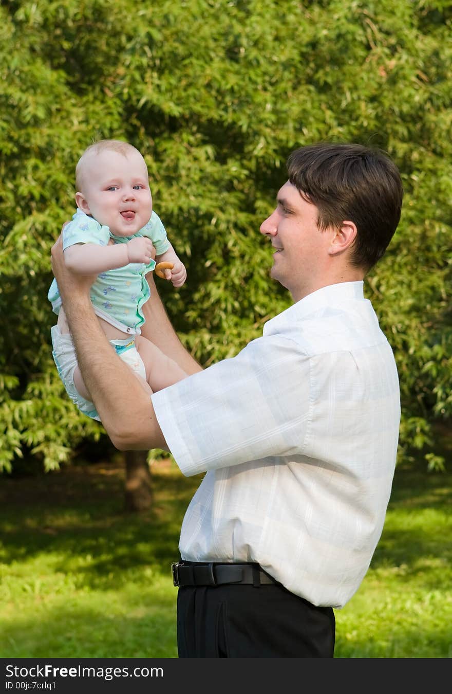 Father holds on hands of the small child on a background of green foliage. Father holds on hands of the small child on a background of green foliage