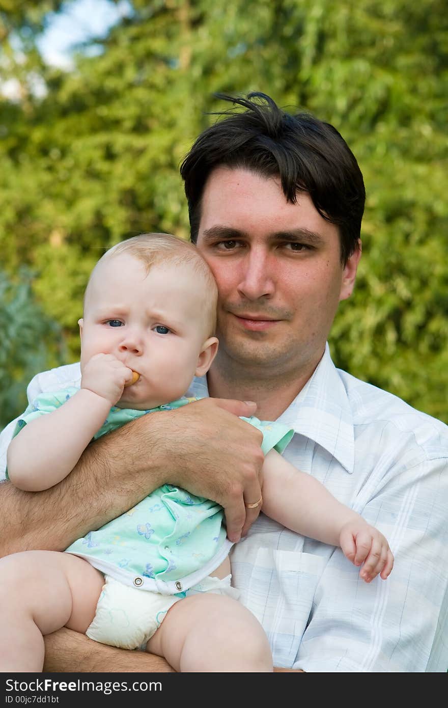 Father holds on hands of the small child on a background of green foliage. Father holds on hands of the small child on a background of green foliage