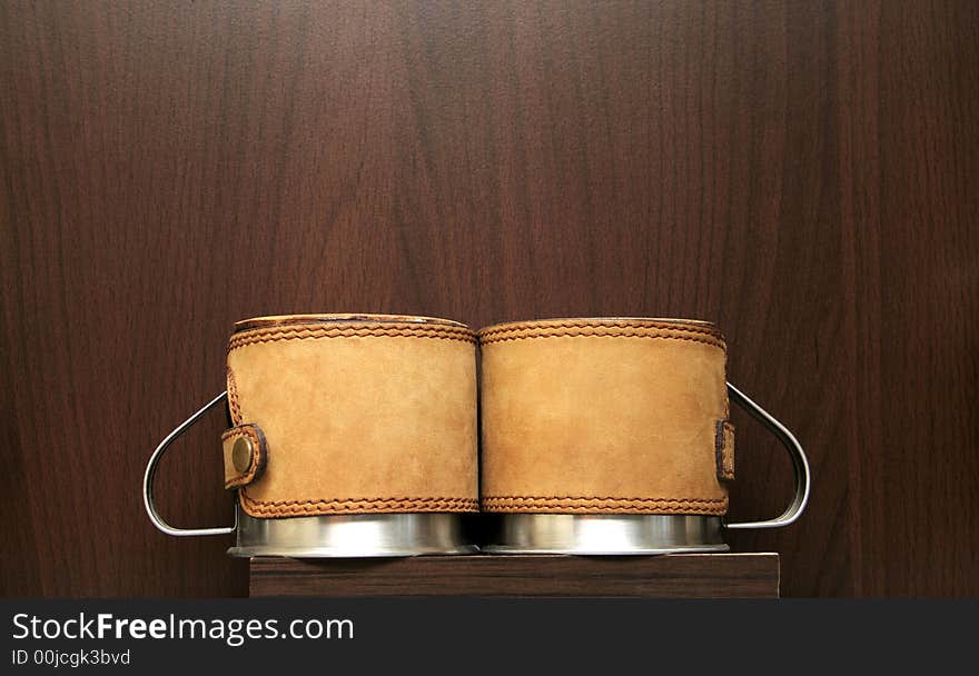 Two silver coffee mugs covered with leather on a brown background