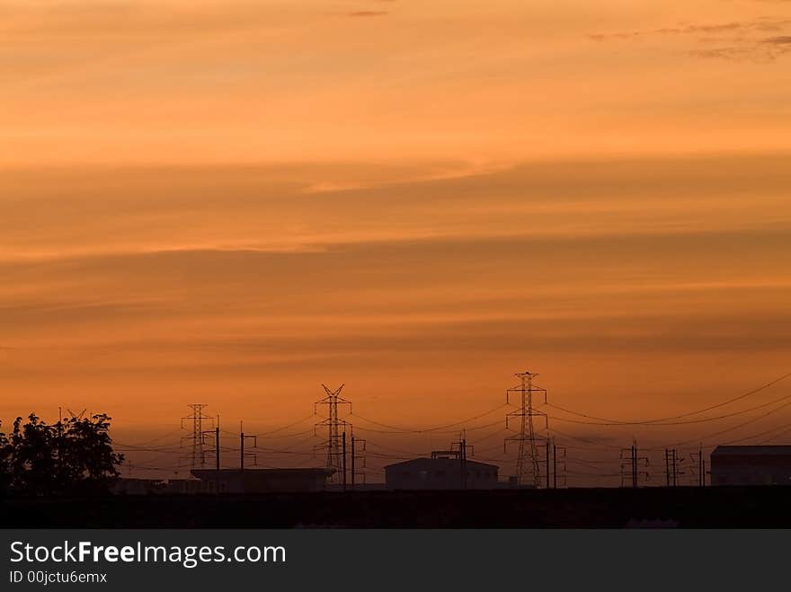 Sunrise in an industrial setting, with the sillhouettes of power lines and industrial buildings. Sunrise in an industrial setting, with the sillhouettes of power lines and industrial buildings.