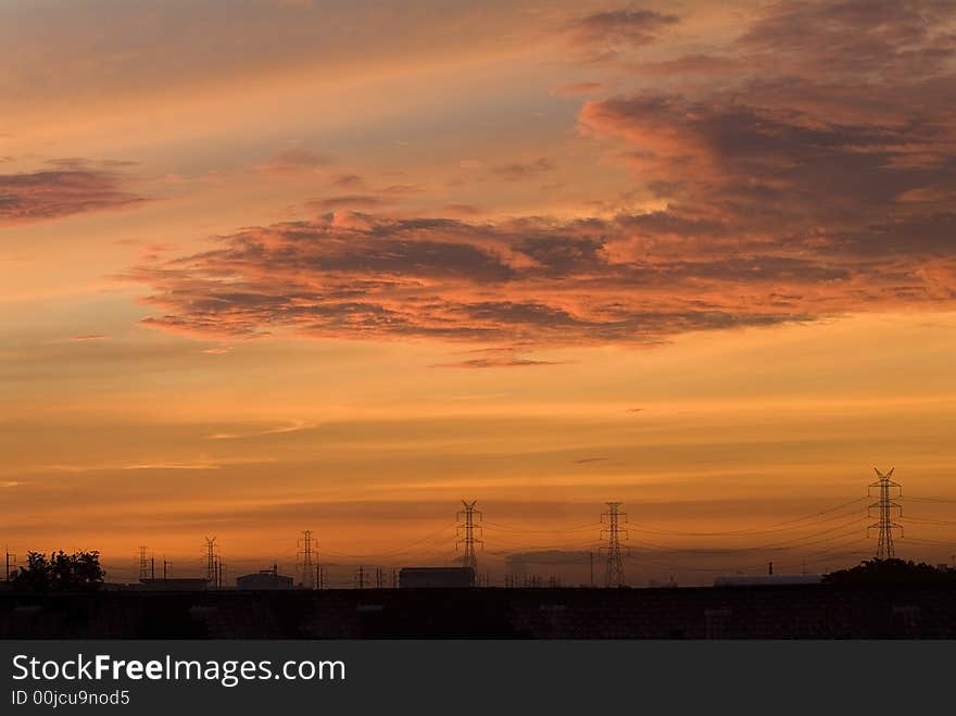 Sunrise in an industrial setting, with the silhouettes of power lines and industrial buildings. Sunrise in an industrial setting, with the silhouettes of power lines and industrial buildings.