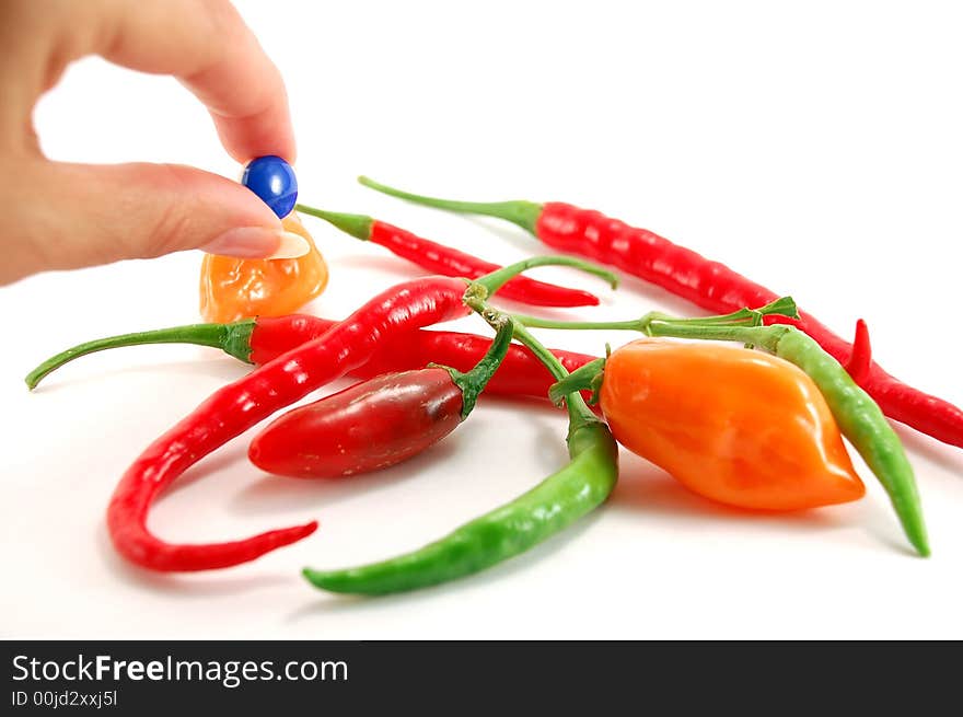 Fingers holding medication next to hot chili peppers. Fingers holding medication next to hot chili peppers