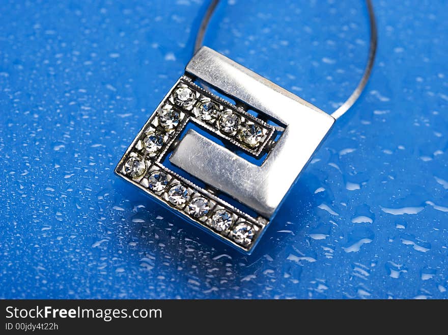 Beautiful silver necklace with diamonds on blue background with water drops