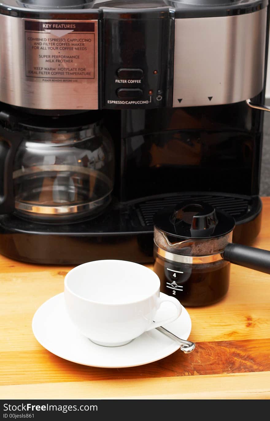 White cup with coffee machine and a freshly brewed pot of coffee in the background. White cup with coffee machine and a freshly brewed pot of coffee in the background