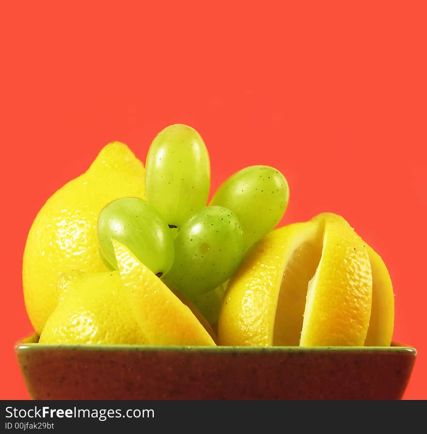 Lemons and grapes fruit in green bowl on red background