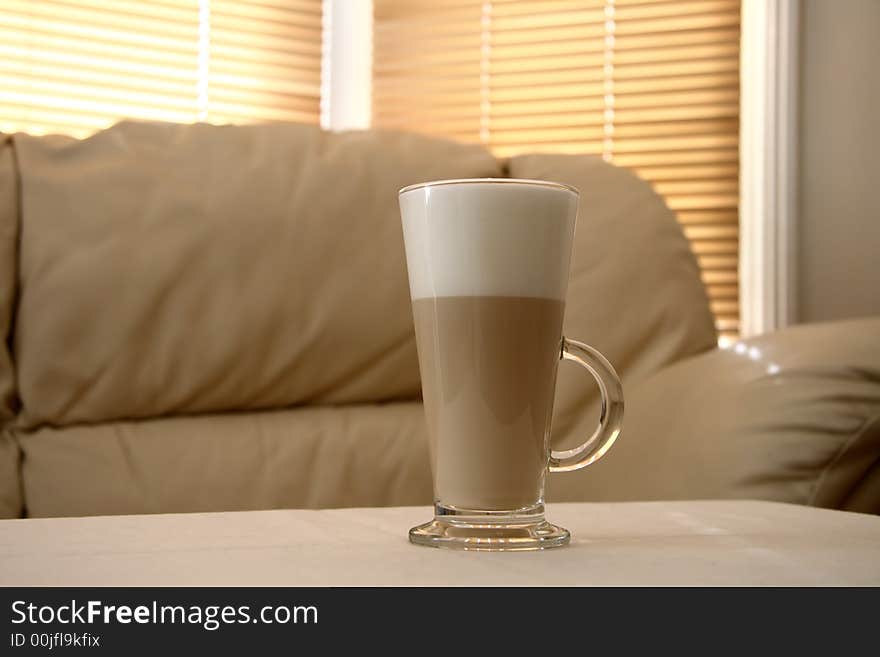 Cafe Latte in a tall glass and creamy sofa on background, soft focus