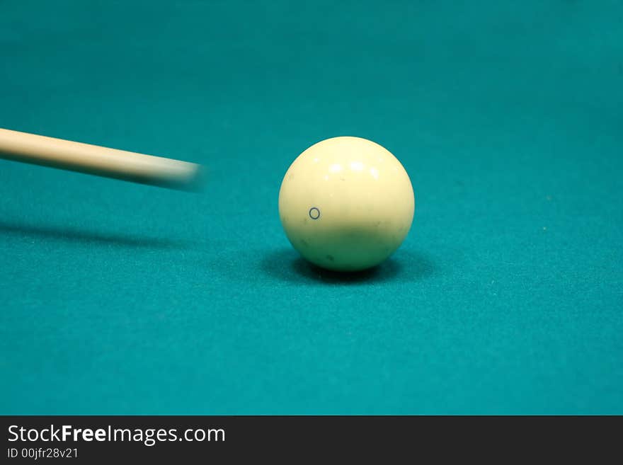 Pool stick striking cue ball on a green table