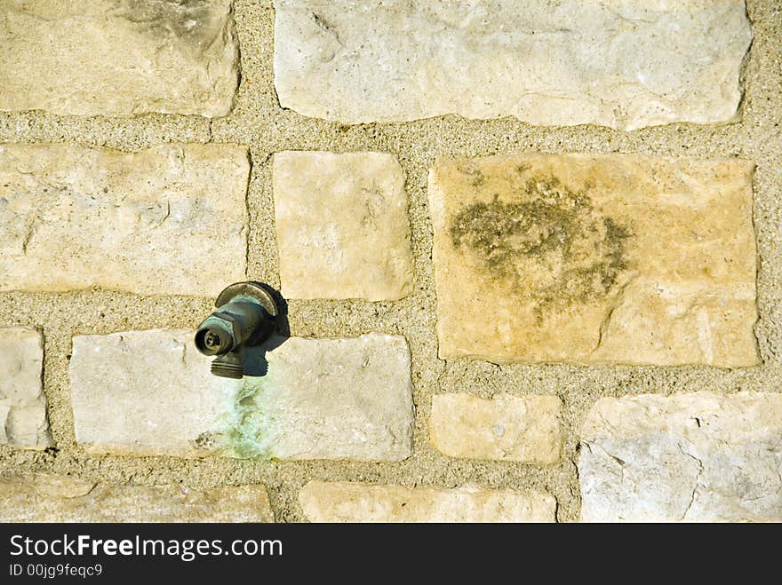 A broken water spout on a yellow block wall.