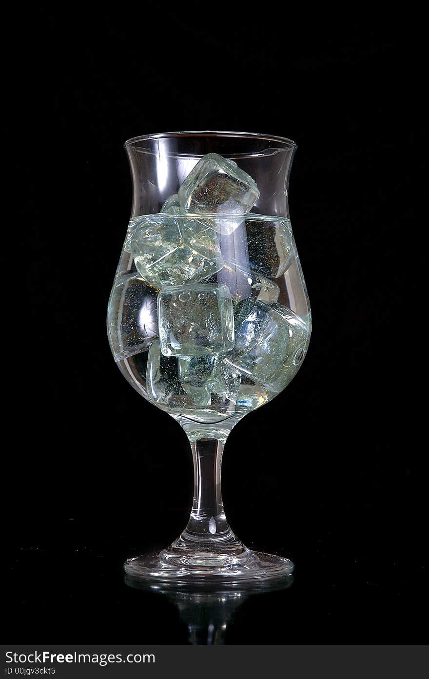 A glass filled with ice cubes and water. Black background.