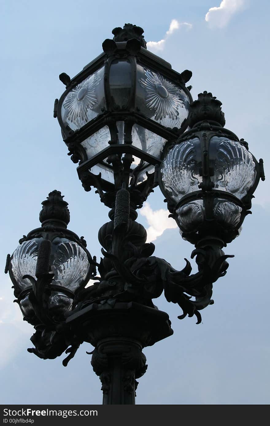 Lamp post in Paris made of forged iron and glass with a cloudy blue sky behind. It's on the Alexandre III bridge. Lamp post in Paris made of forged iron and glass with a cloudy blue sky behind. It's on the Alexandre III bridge.