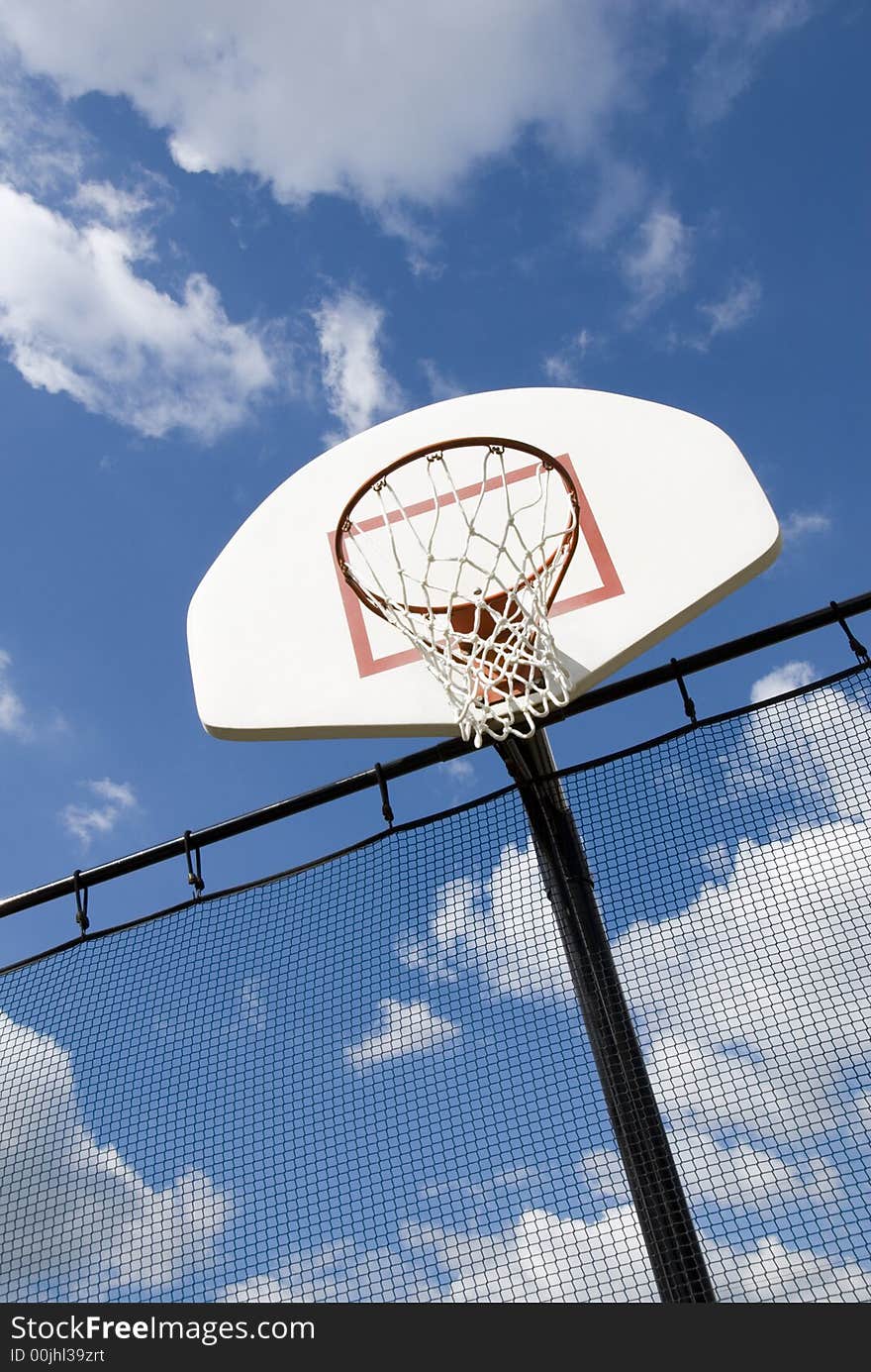 A basketball hoop in a children's playground stands against a partly cloudy blue sky.