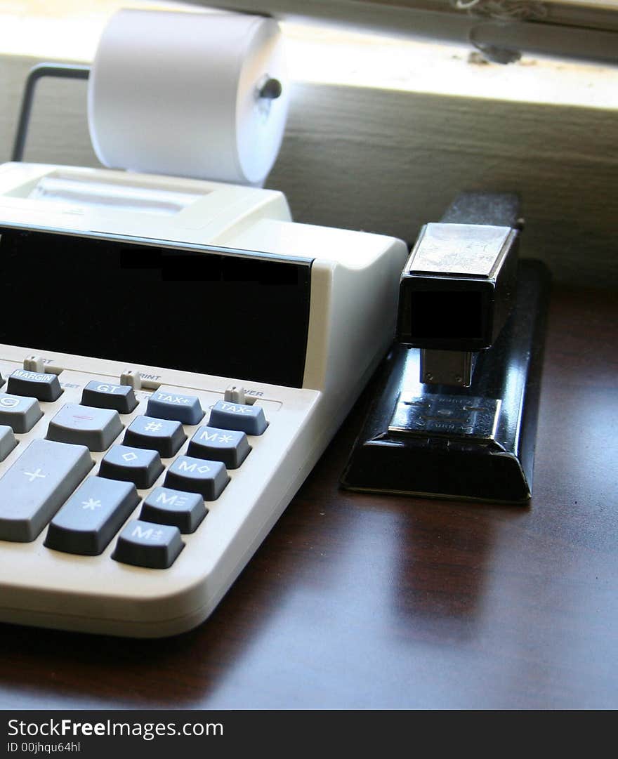 Calculator and a stapeler on a deskin front of window. Calculator and a stapeler on a deskin front of window