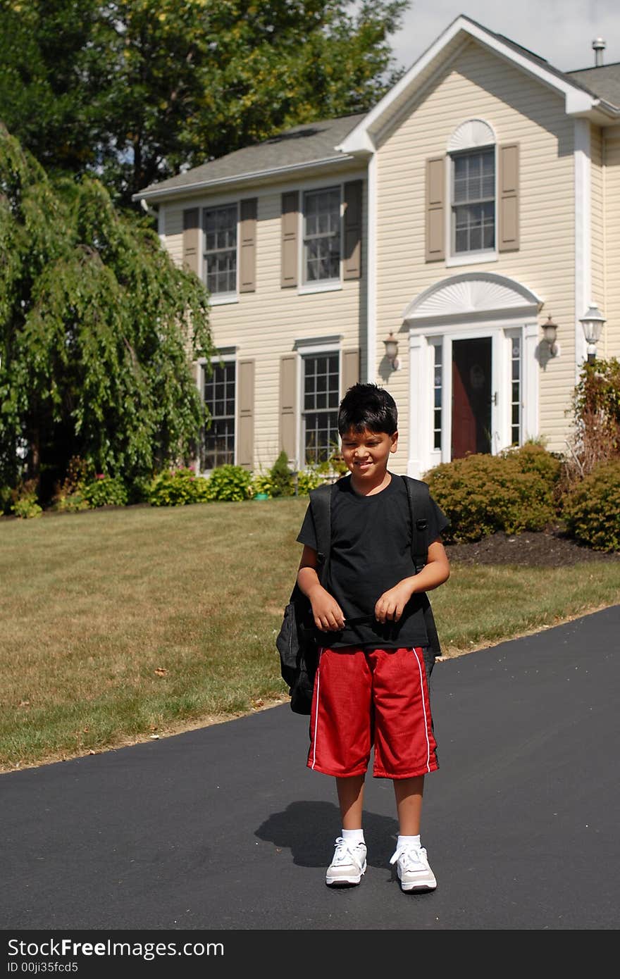 Elementary boy waiting for the school bus in front of his house.