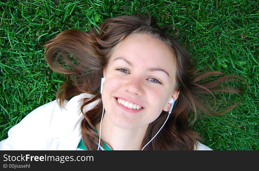 Young girl laying on the green grass and listening music