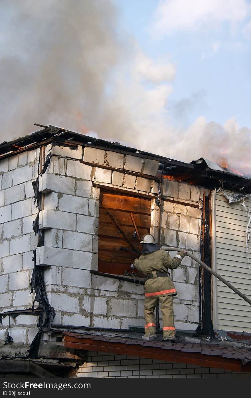 Firefighter extinguishing a fire in flaming house. Firefighter extinguishing a fire in flaming house