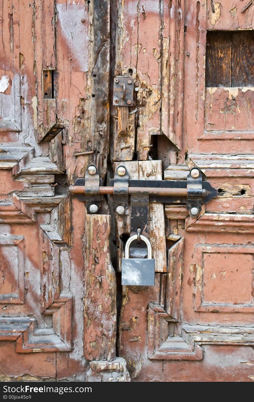 An old wood door with a rusty door latch and a padlock. An old wood door with a rusty door latch and a padlock