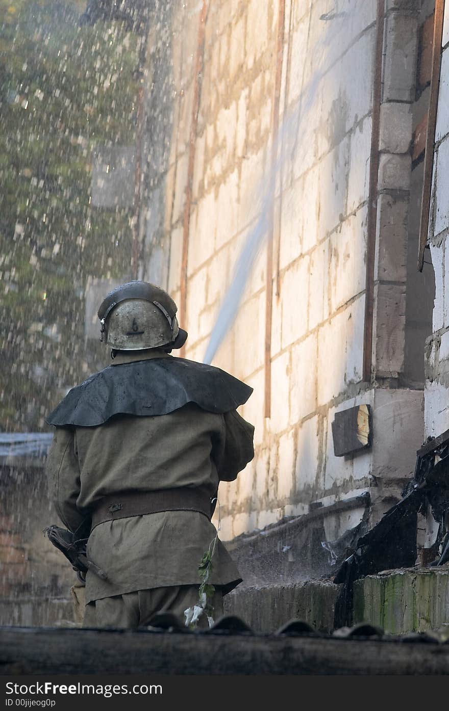 Fireman with fire hose spraying water on a flaming house