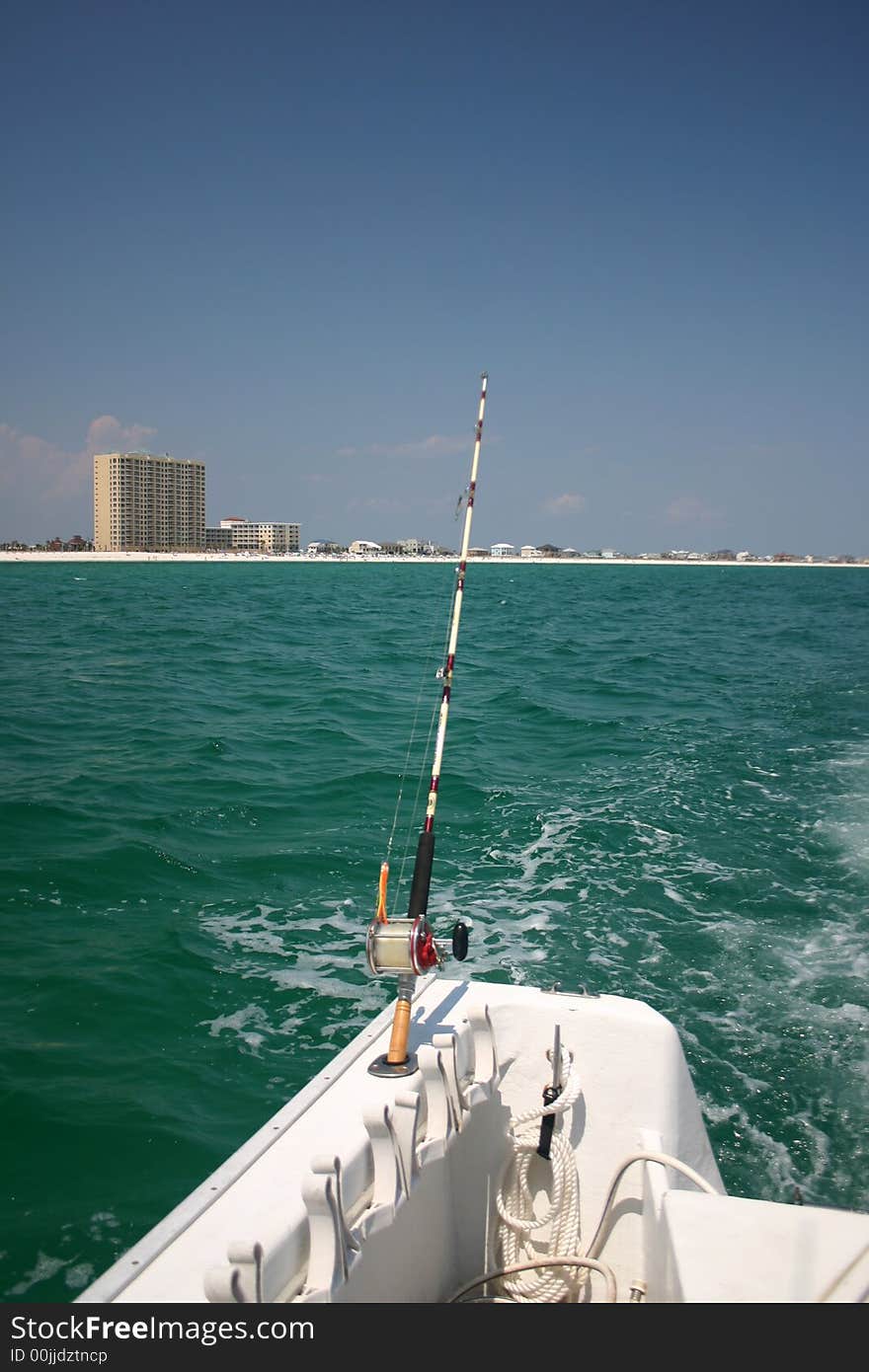 Fishing pole on the back of a boat underway with beachfront in background