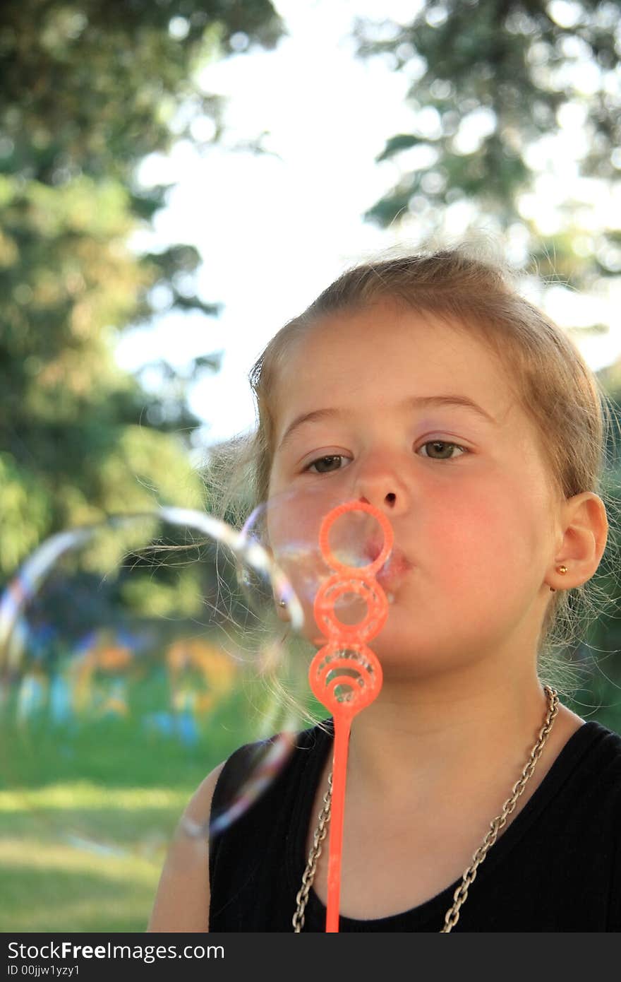 Young girl blowing bubbles with a small wand. Young girl blowing bubbles with a small wand.