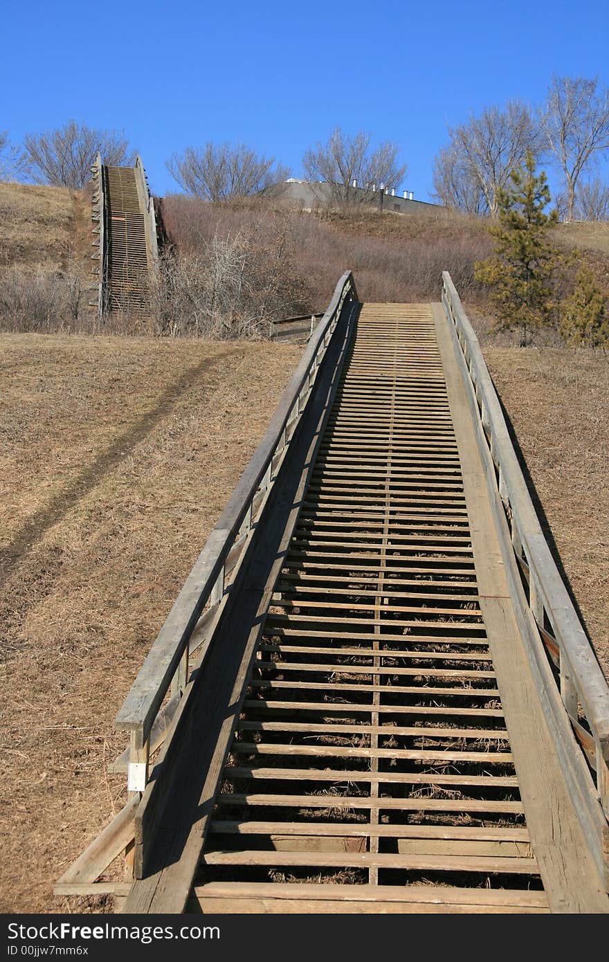 A long double wooden stairway climbing a very tall hill; metaphor for moving up, challenge,reaching for the top. A long double wooden stairway climbing a very tall hill; metaphor for moving up, challenge,reaching for the top.