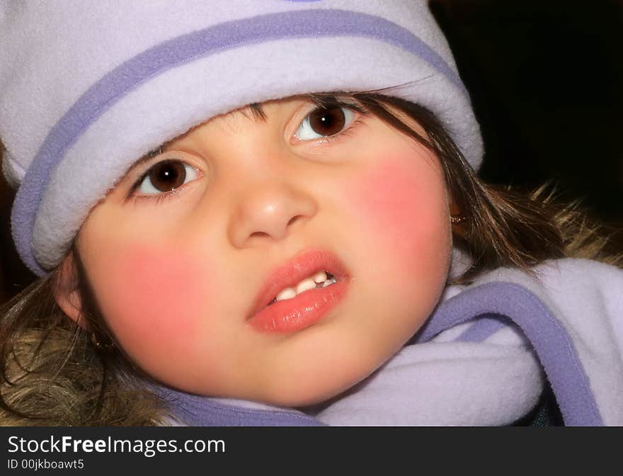 Face of a little girl with rosy cheeks wearing a lilac scarf and hat with a puzzled look on her face.