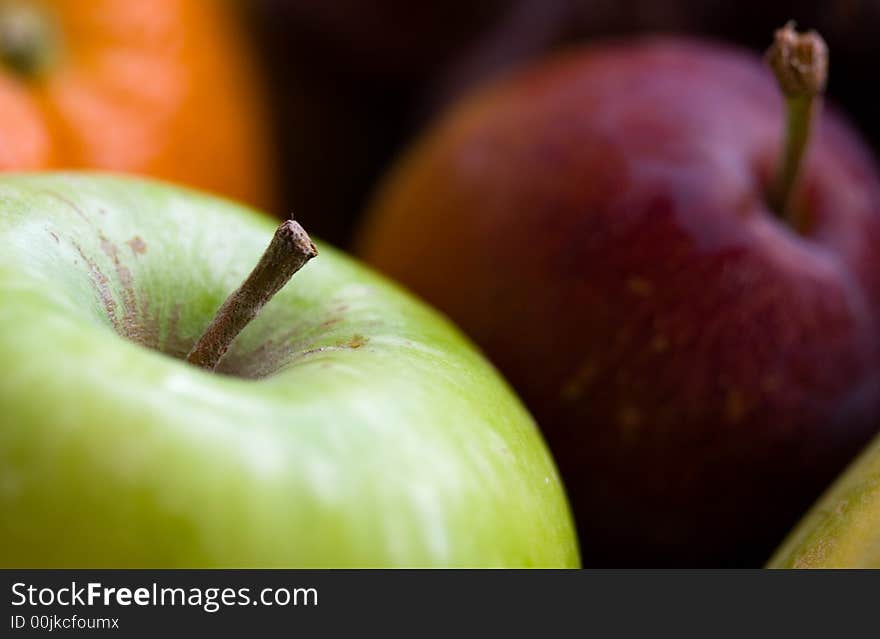 Macro shot of an apple with a plum, orange and papaya in the background. Macro shot of an apple with a plum, orange and papaya in the background