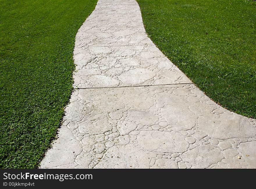 Textured cement pathway diminishing through lush green grass