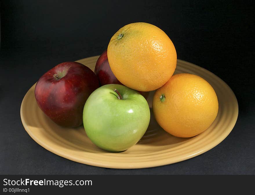 Apples and oranges mixed fruits on yellow plate with dark background. Apples and oranges mixed fruits on yellow plate with dark background