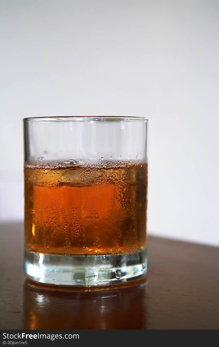 The misted over glass of whisky with an ice on a table