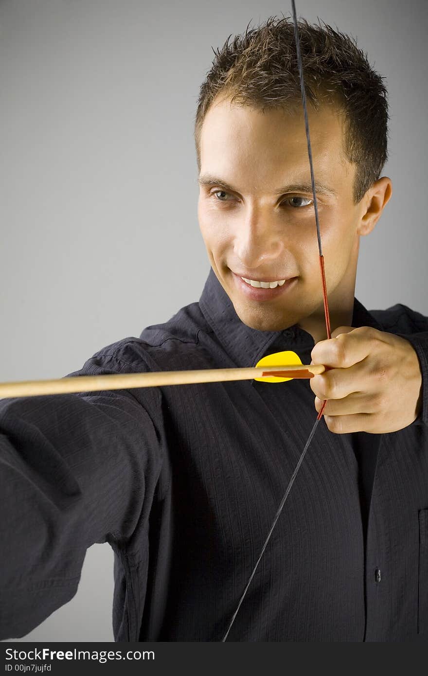 Young, elegant man in black shirt holding bow. Smiling and shooting to target. Gray background. Young, elegant man in black shirt holding bow. Smiling and shooting to target. Gray background