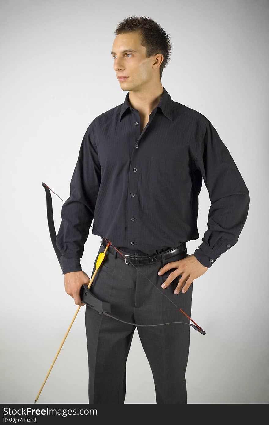 Young, elegant man in black shirt holding bow. Looking at something. Gray background. Young, elegant man in black shirt holding bow. Looking at something. Gray background