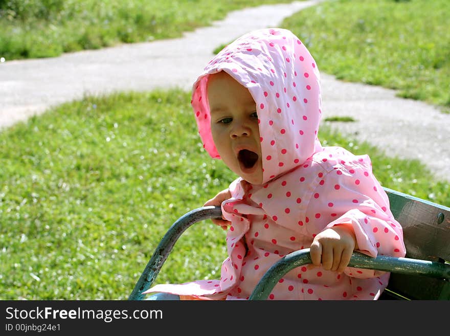 Little baby sitting on the carousel and yawning. There is green grass and crossroad on the backstage. Little baby sitting on the carousel and yawning. There is green grass and crossroad on the backstage