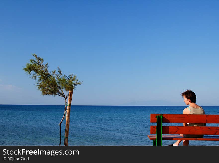 Young girl on a banch on the coast with a small tree