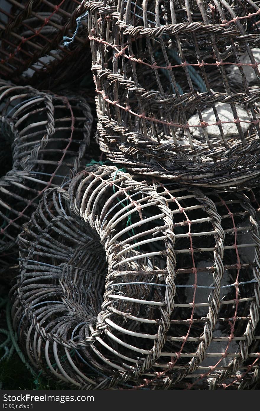 A bunch of fishing traps, stacked on top of one another. they are made of metal and rope woven together. The colors are grey, whites, turquoise, and rust.