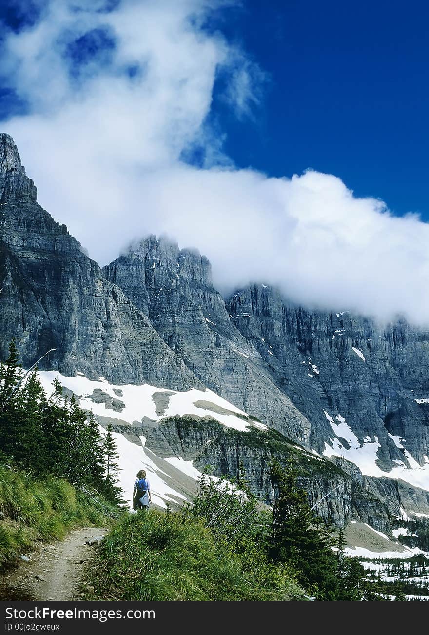 Female Hiker on mountain trail with dramatic peaks and swirling clouds against dark blue sky. Female Hiker on mountain trail with dramatic peaks and swirling clouds against dark blue sky