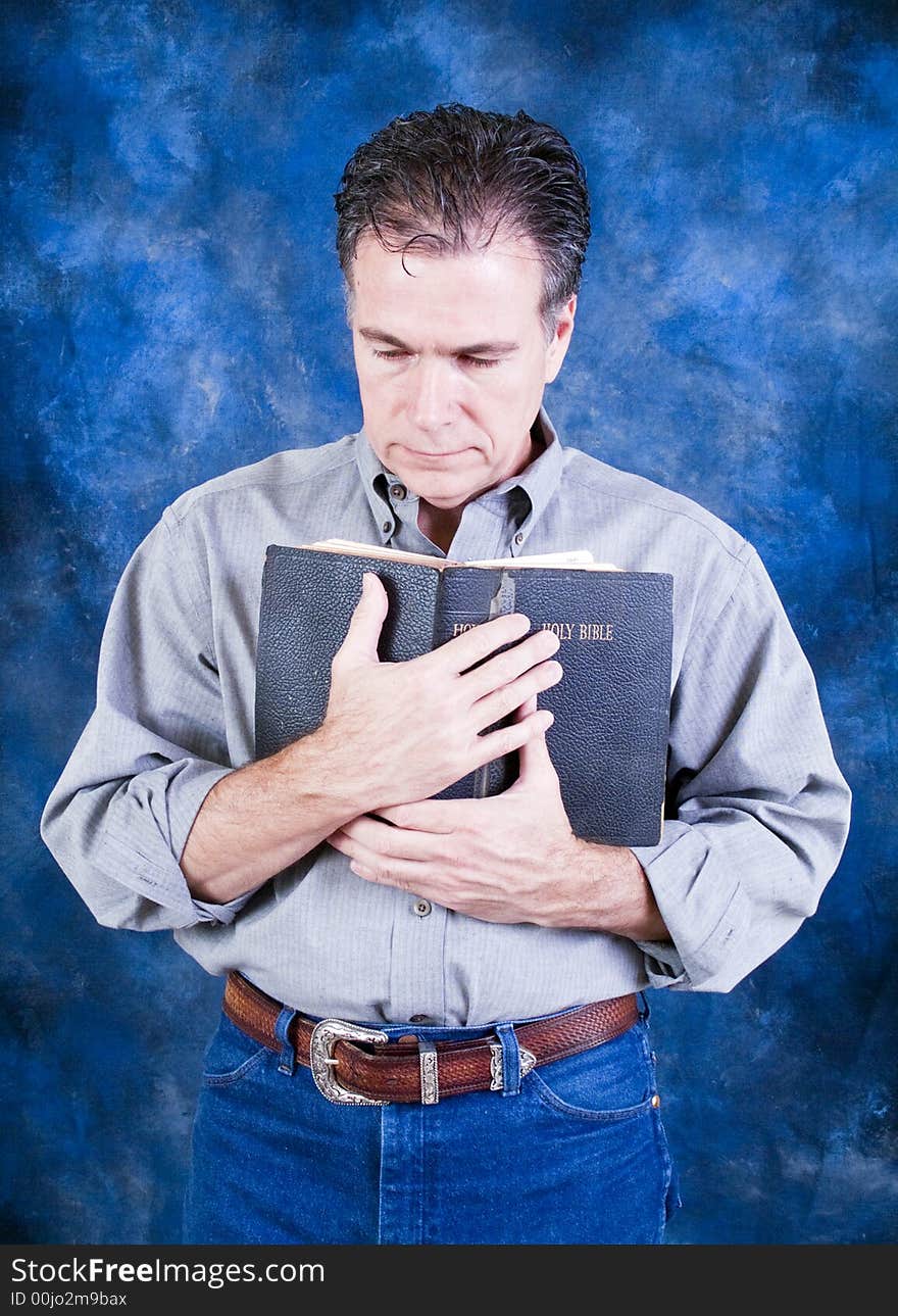 A man standing and tenderly holding an old bible to his chest. A man standing and tenderly holding an old bible to his chest.