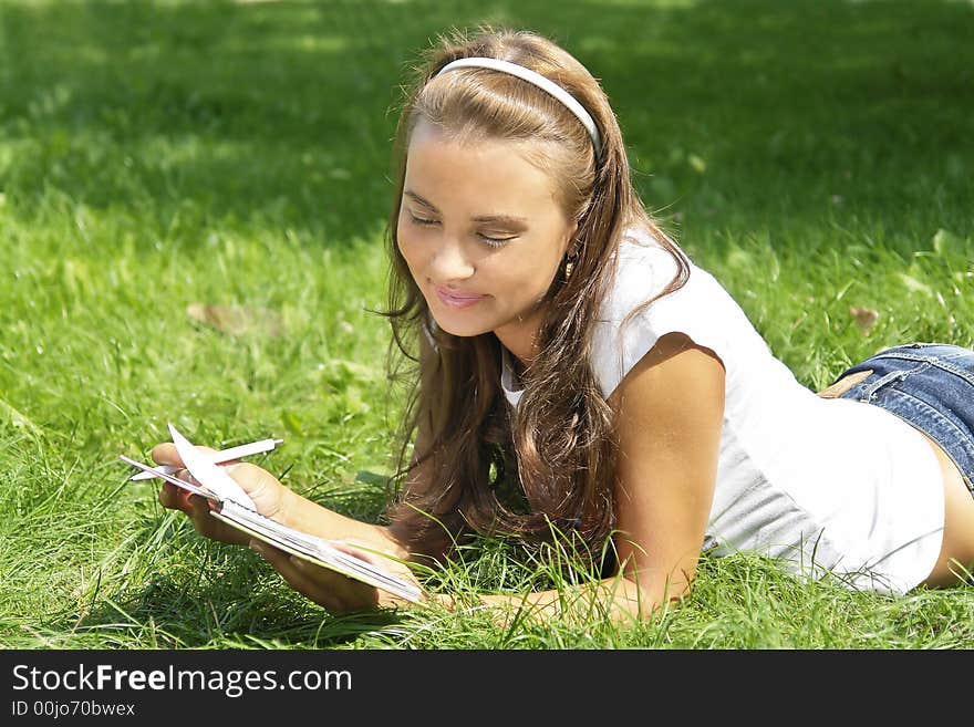 Beautiful young girl reading notes on the grass