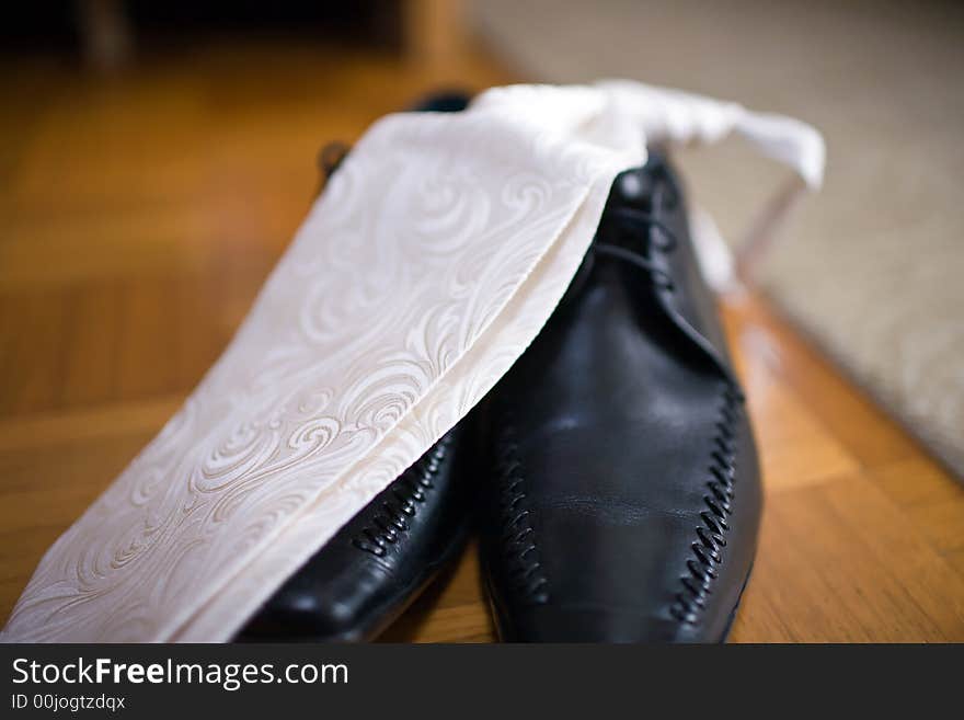 Festive, light-coloured Necktie on black Leathershoes. Standing on Parquet. Close-up with very shallow DOF. Festive, light-coloured Necktie on black Leathershoes. Standing on Parquet. Close-up with very shallow DOF.