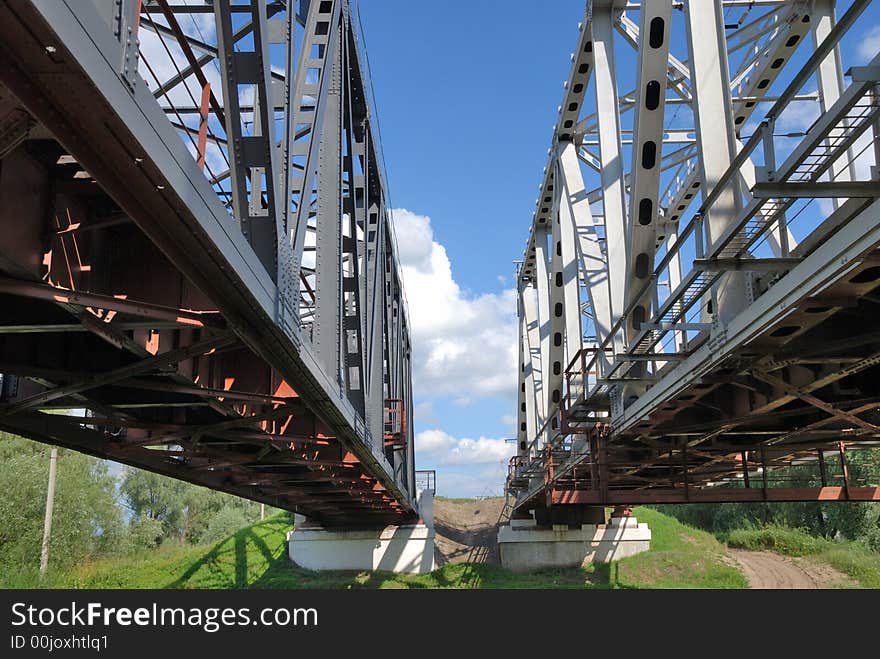 Grey railway bridge and the cloudy summer sky