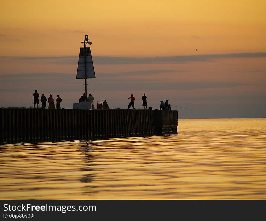 Several people gather on the end of the pier to watch the sun go down over the lake. Several people gather on the end of the pier to watch the sun go down over the lake.