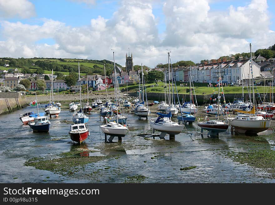 Sailing boats at anchor in a small harbour with the tide out and colorful houses to the rear. Location Aberaeron, Wales, United Kingdom.