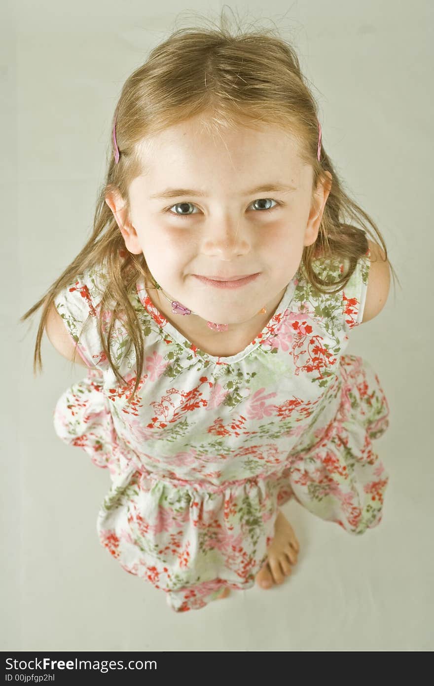 Bird's eye portrait of a smiling young girl in a print dress. Plain background, isolated, vertical.