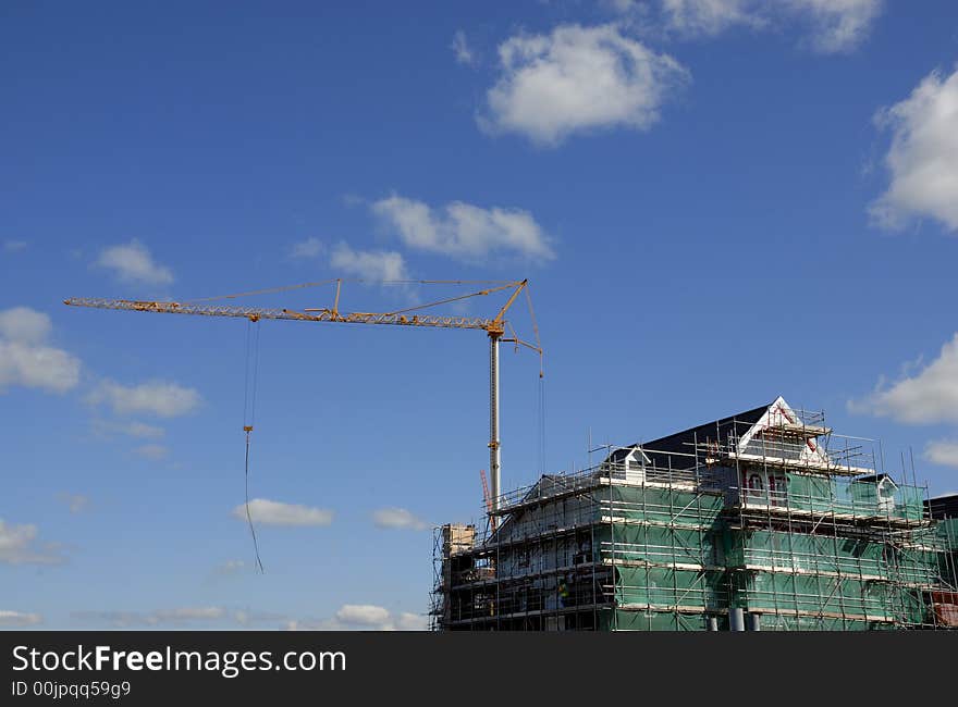 Tall crane against a blue sky with a construction site surrounded with scaffolding and plenty of copy space. Tall crane against a blue sky with a construction site surrounded with scaffolding and plenty of copy space