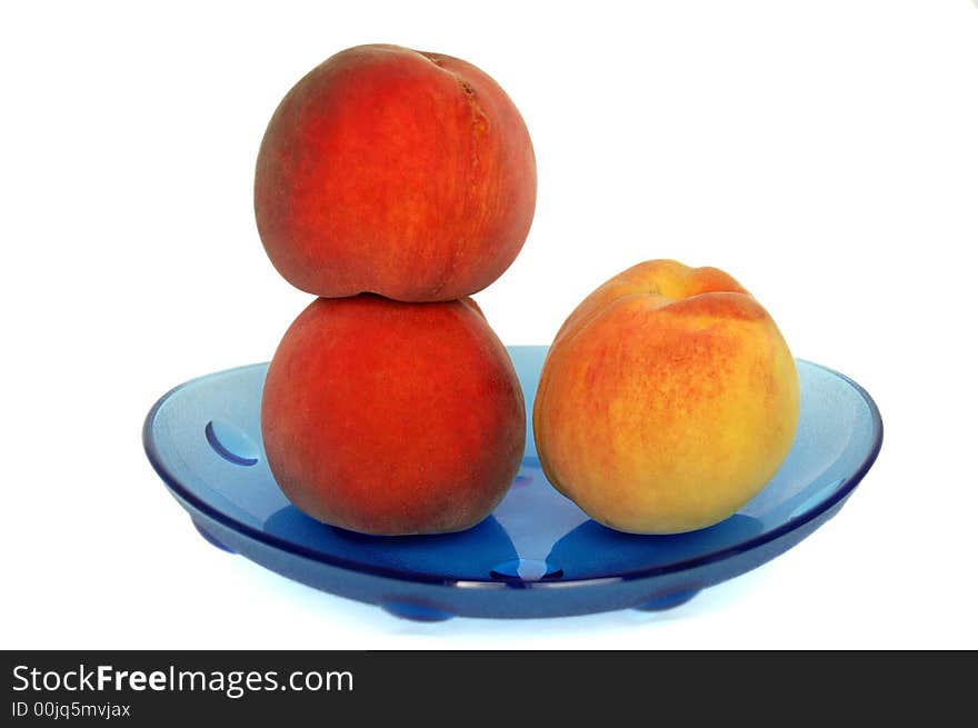 Three peaches on a blue plate. White background.