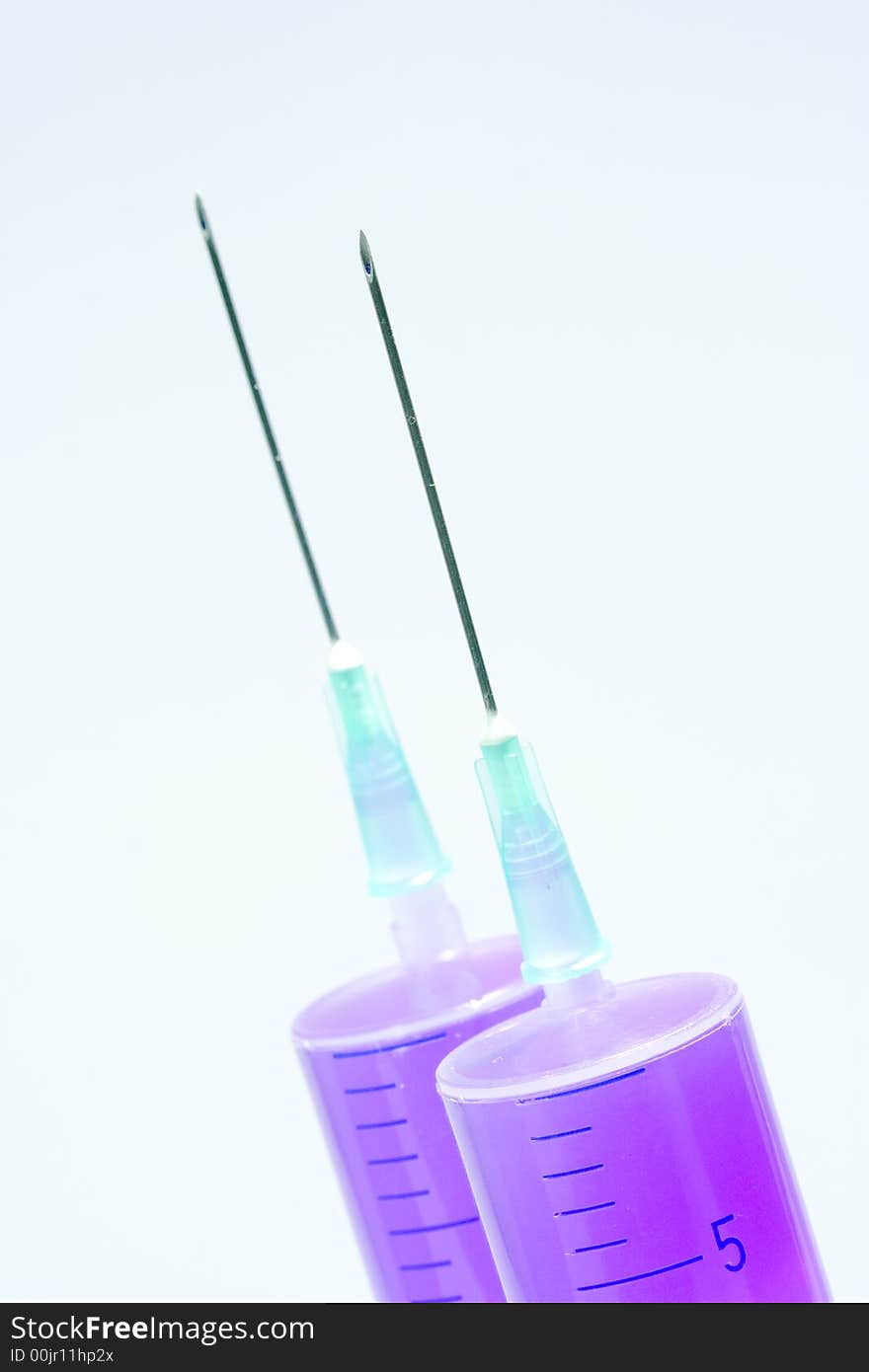 Two disposable syringes filled with purple fluid with needles against the white background. Two disposable syringes filled with purple fluid with needles against the white background