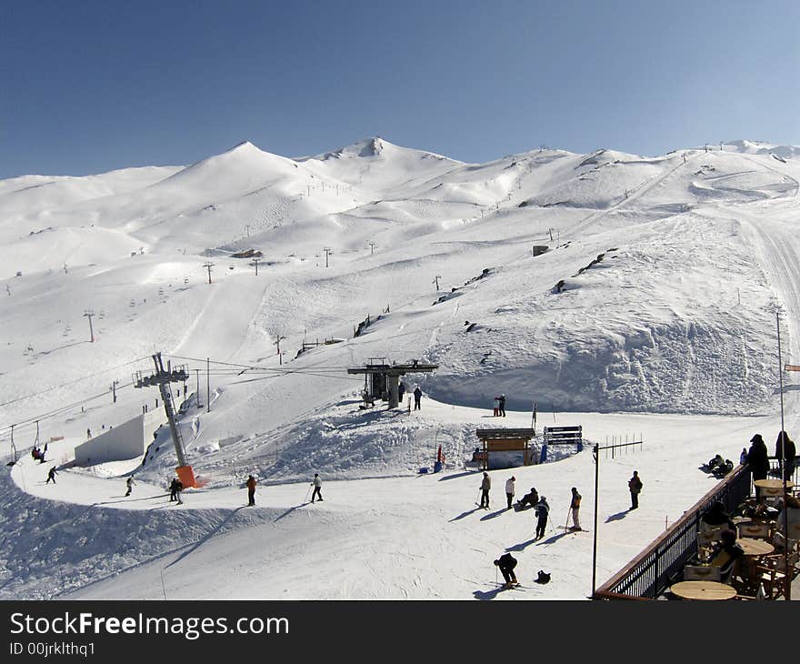 People enjoy a perfect day skiing down the slopes while others watch from the balcony of the resort. People enjoy a perfect day skiing down the slopes while others watch from the balcony of the resort