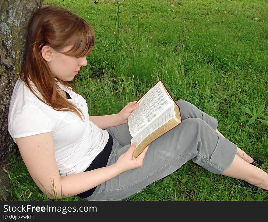 A teenage girl reads by a tree. A teenage girl reads by a tree.